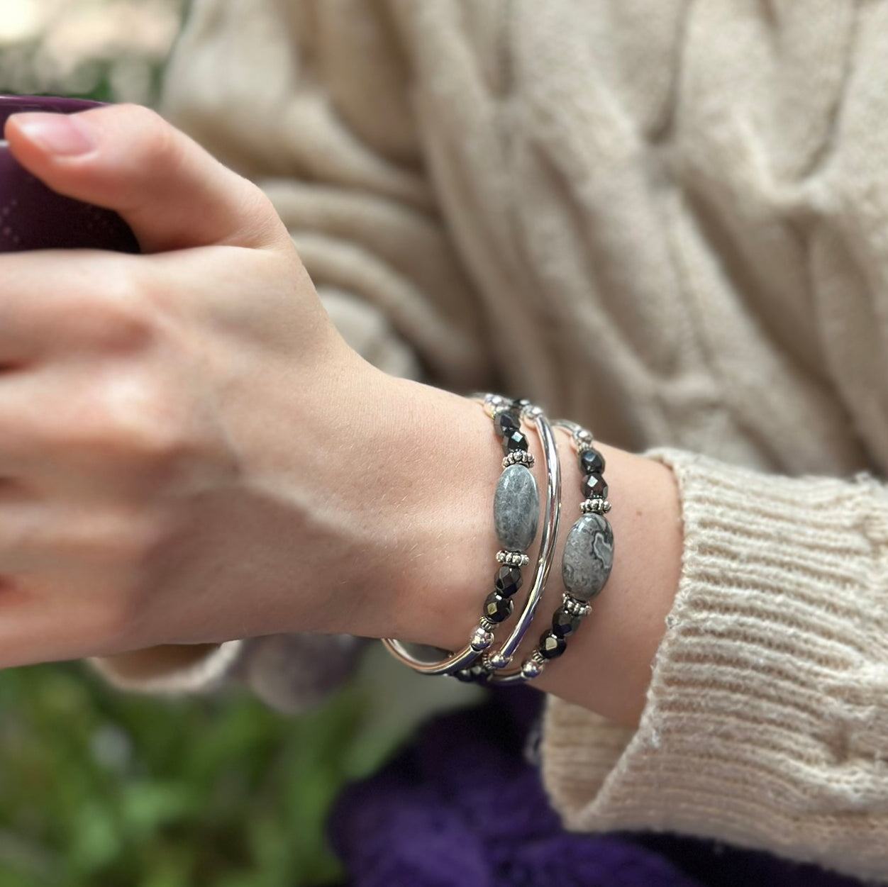 Close-up of a person's wrist wearing multiple bracelets with a blurred natural background