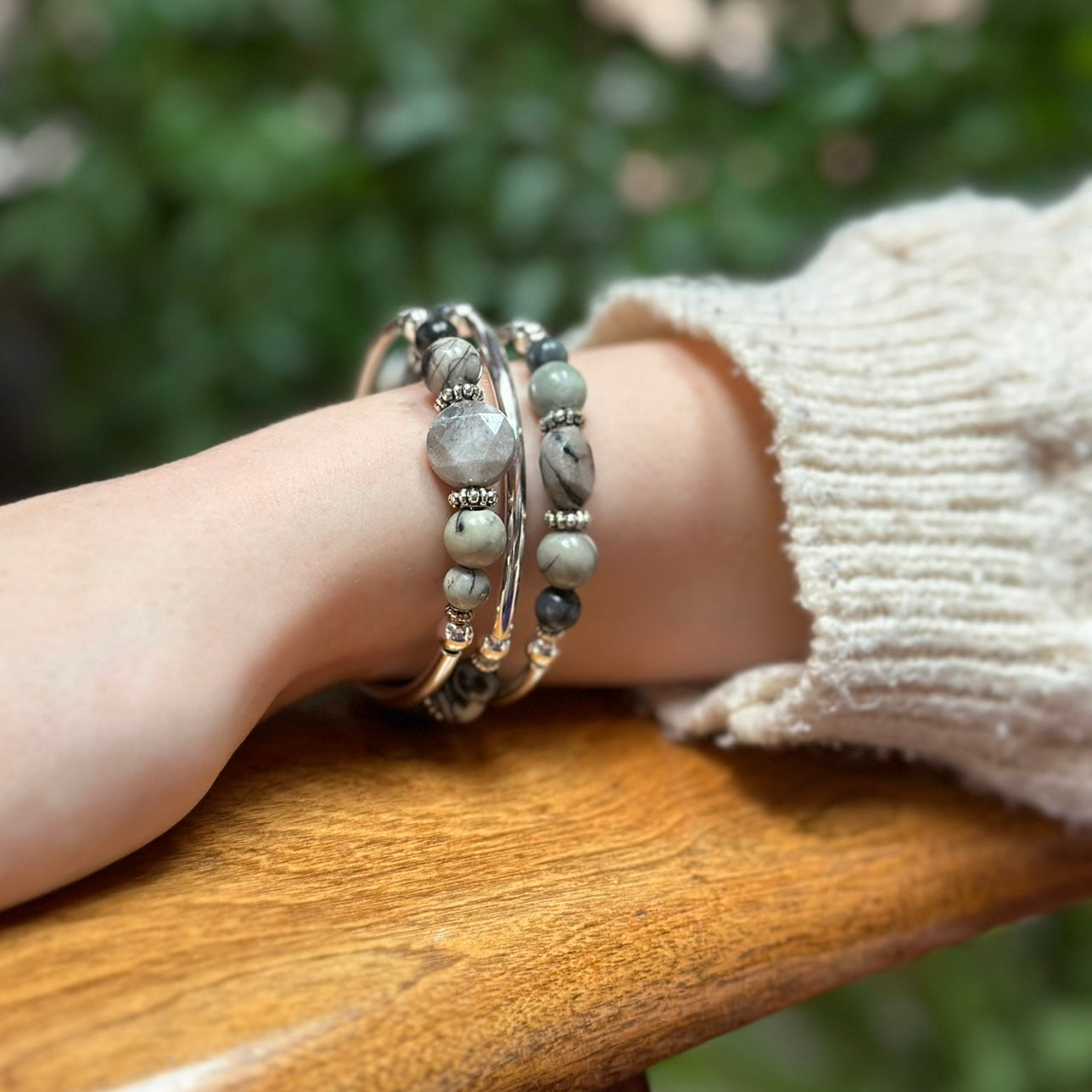 Close-up of a wrist wearing multiple bracelets on a wooden surface with a blurred natural background