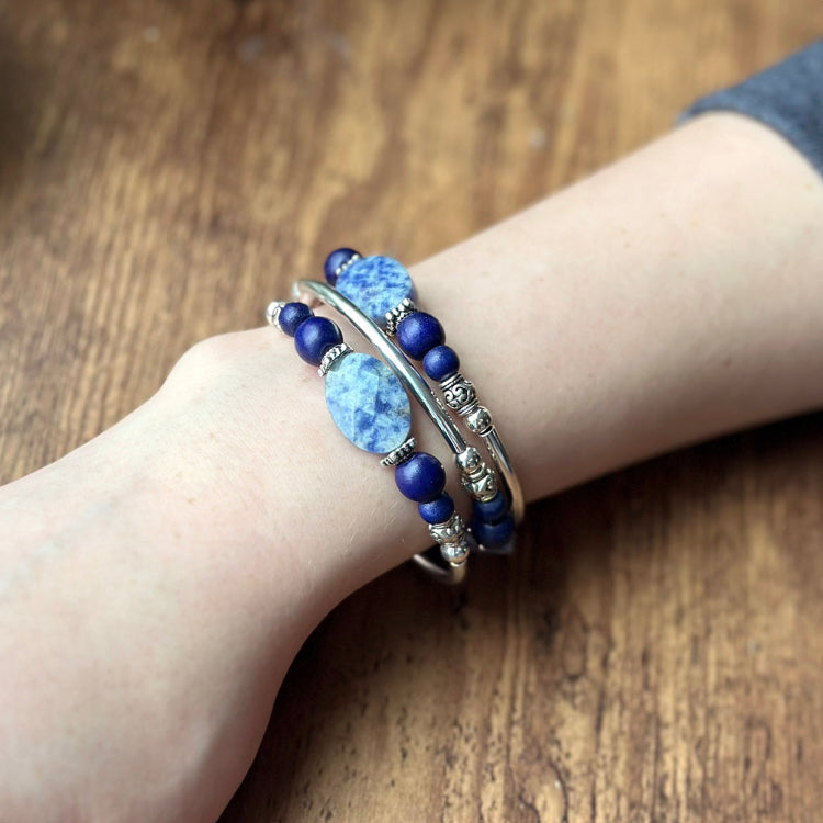 Close-up of a wrist wearing multiple blue beaded bracelets on a wooden surface