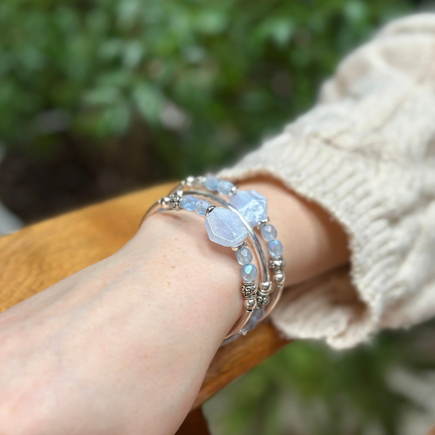 Hand wearing a stack of opal beaded bracelets with a blurred green background