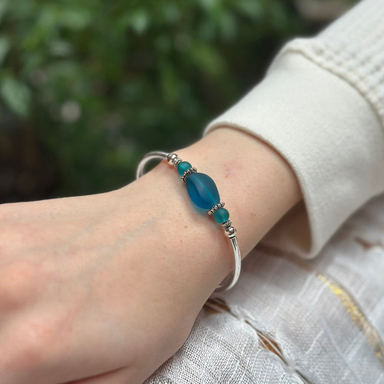 Hand wearing a blue beaded bracelet with a blurred green background