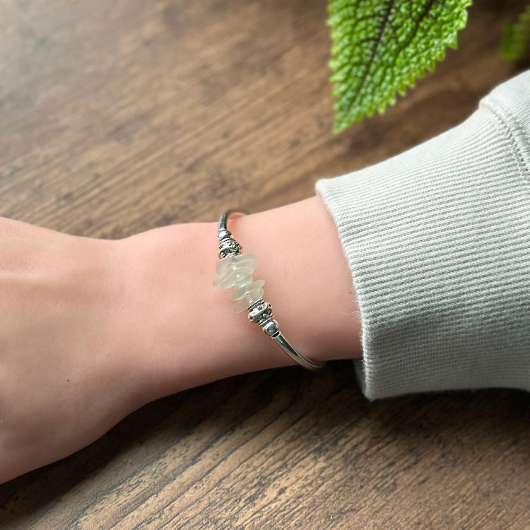 Silver bracelet with a green stone on a wrist against a wooden background
