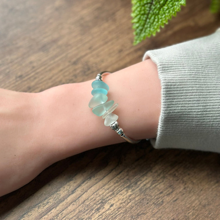 Hand wearing a bracelet with light blue beads on a wooden surface