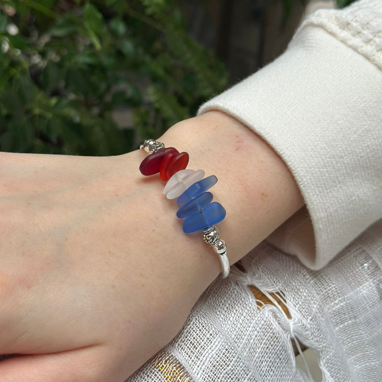 Bracelet with red, white, and blue beads on a wrist against a blurred natural background