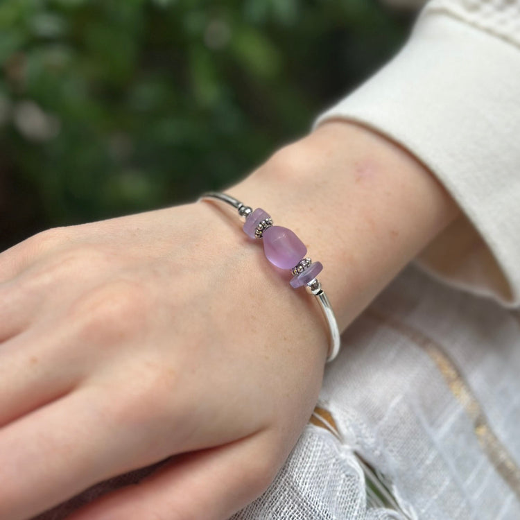 Hand wearing a bracelet with a purple bead against a blurred green background