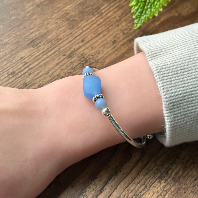 Silver bracelet with blue beads on a wrist against a wooden background