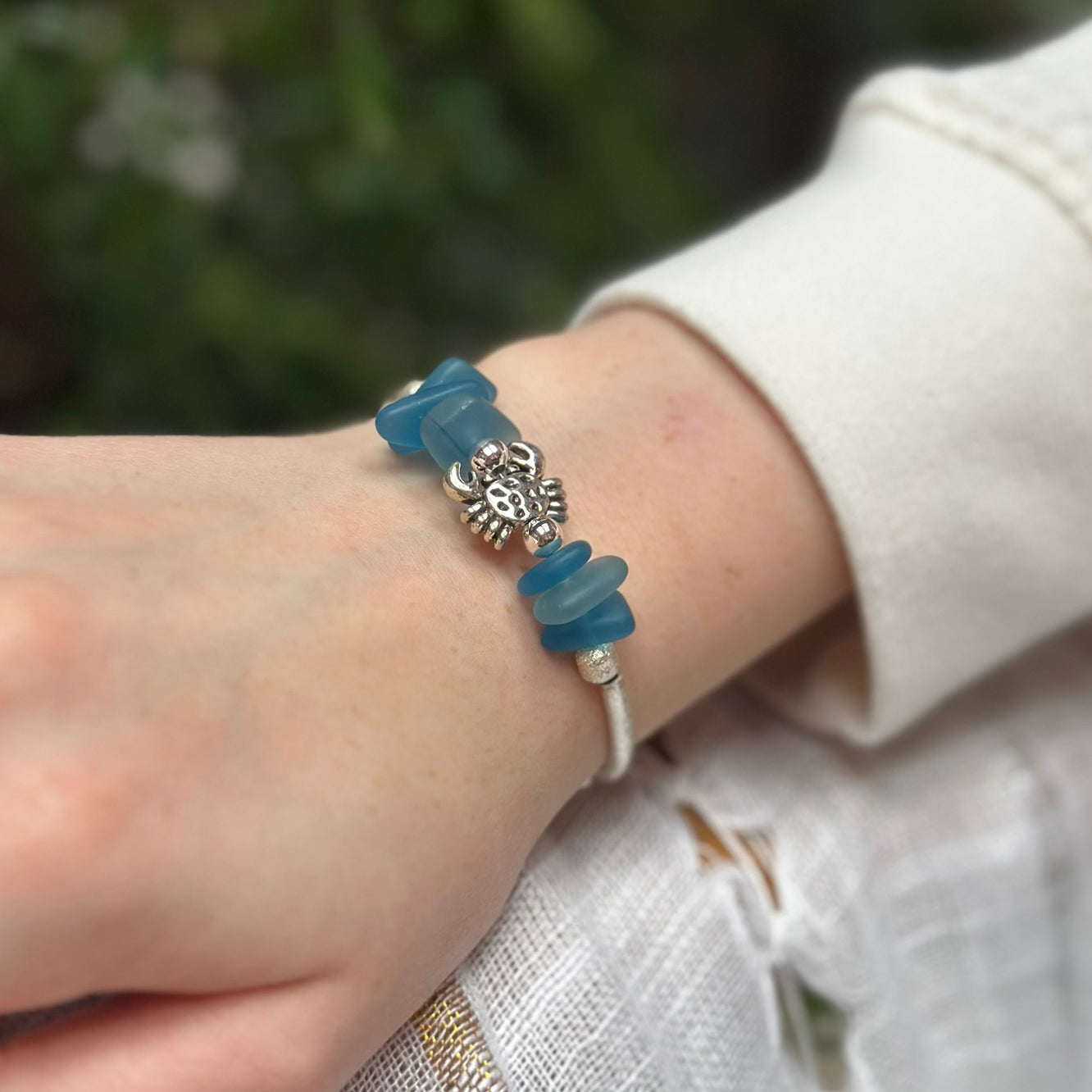 Silver bracelet with blue beads and a crab charm on a wrist