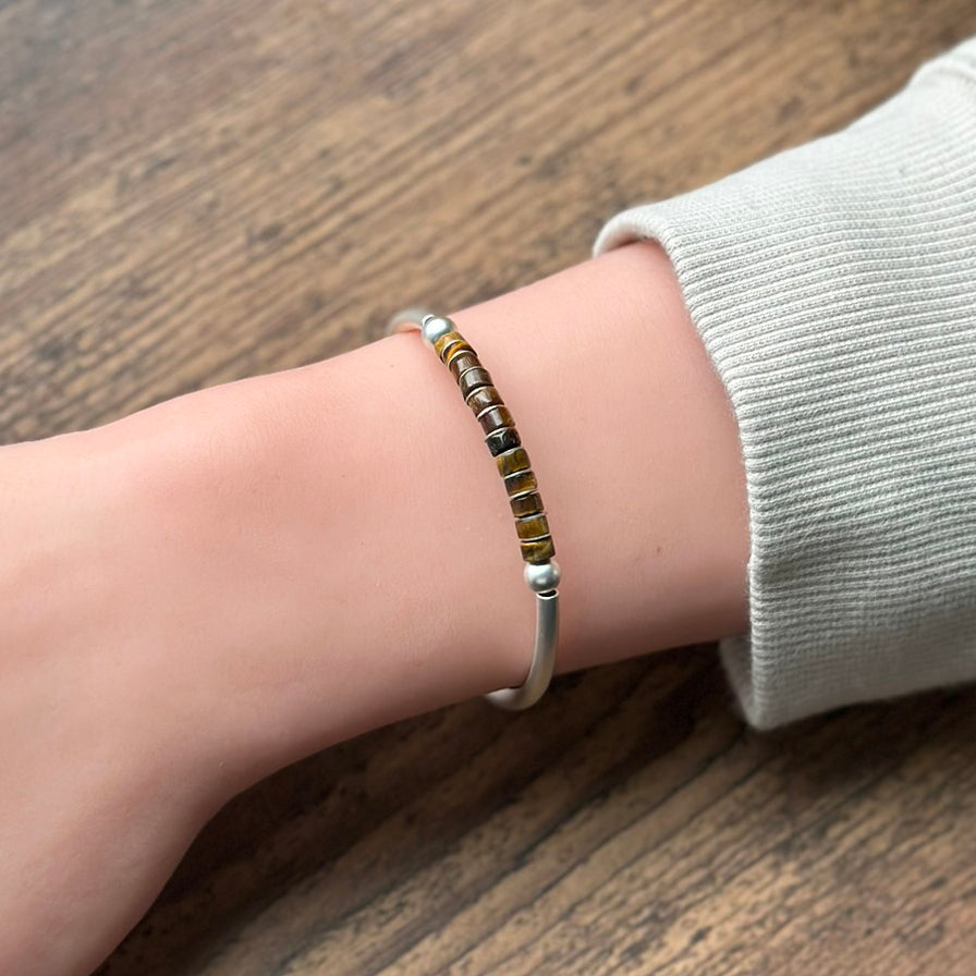 Silver bracelet with brown beads on a wrist with a wood toned background