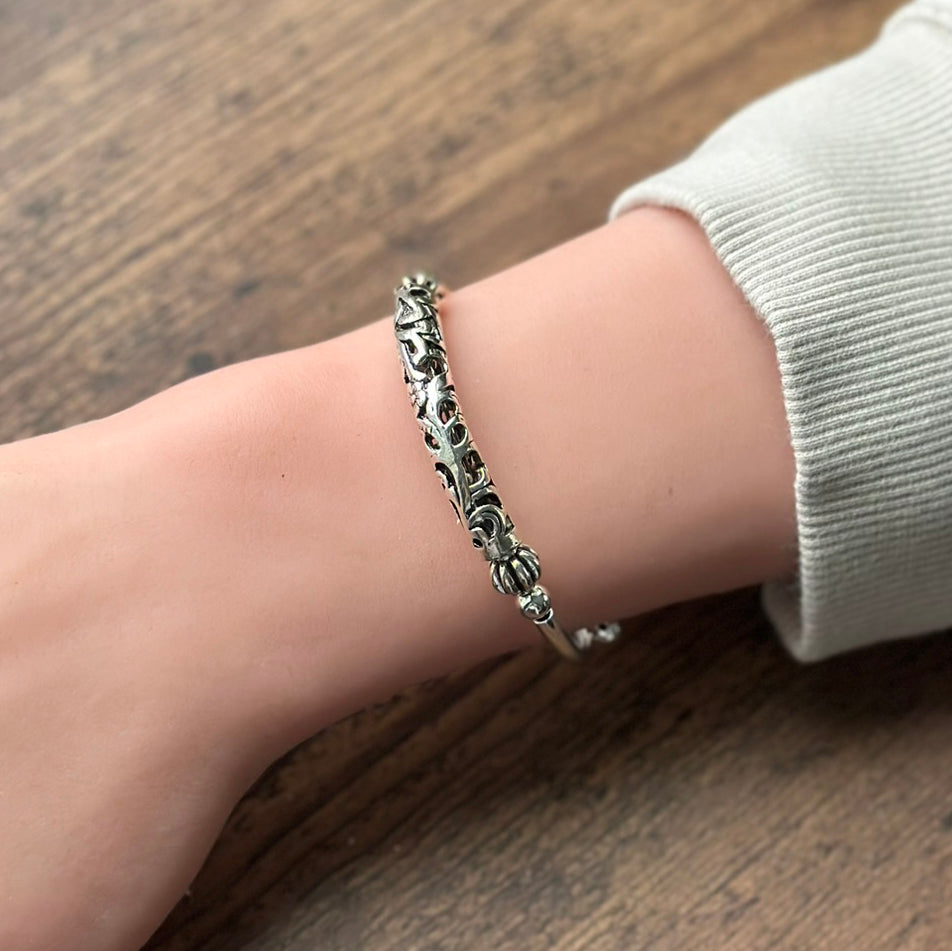 Silver carved tube bracelet on a wrist with a wood toned background