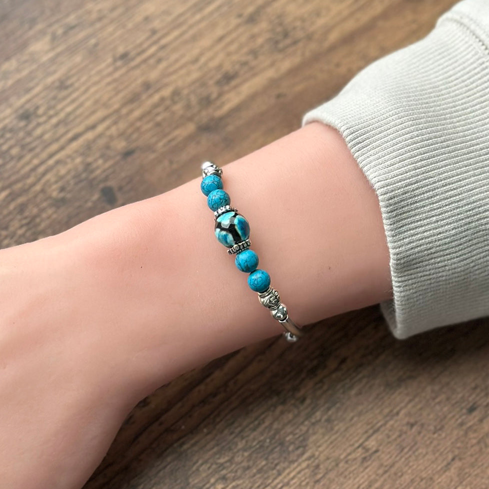 blue and black bracelet with silver accents on a wrist with a wood toned background