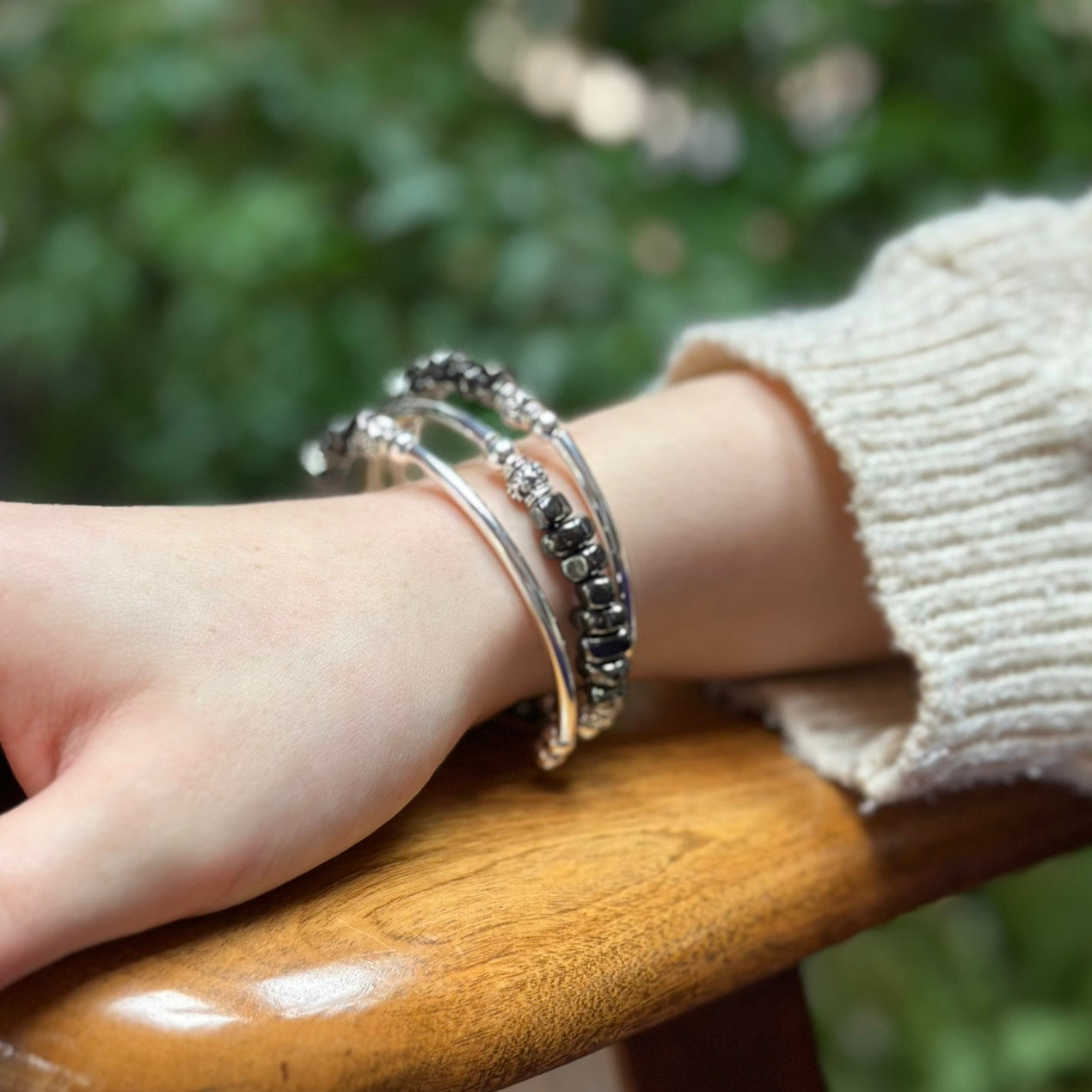Close-up of a wrist wearing multiple silver bracelets with a blurred green background