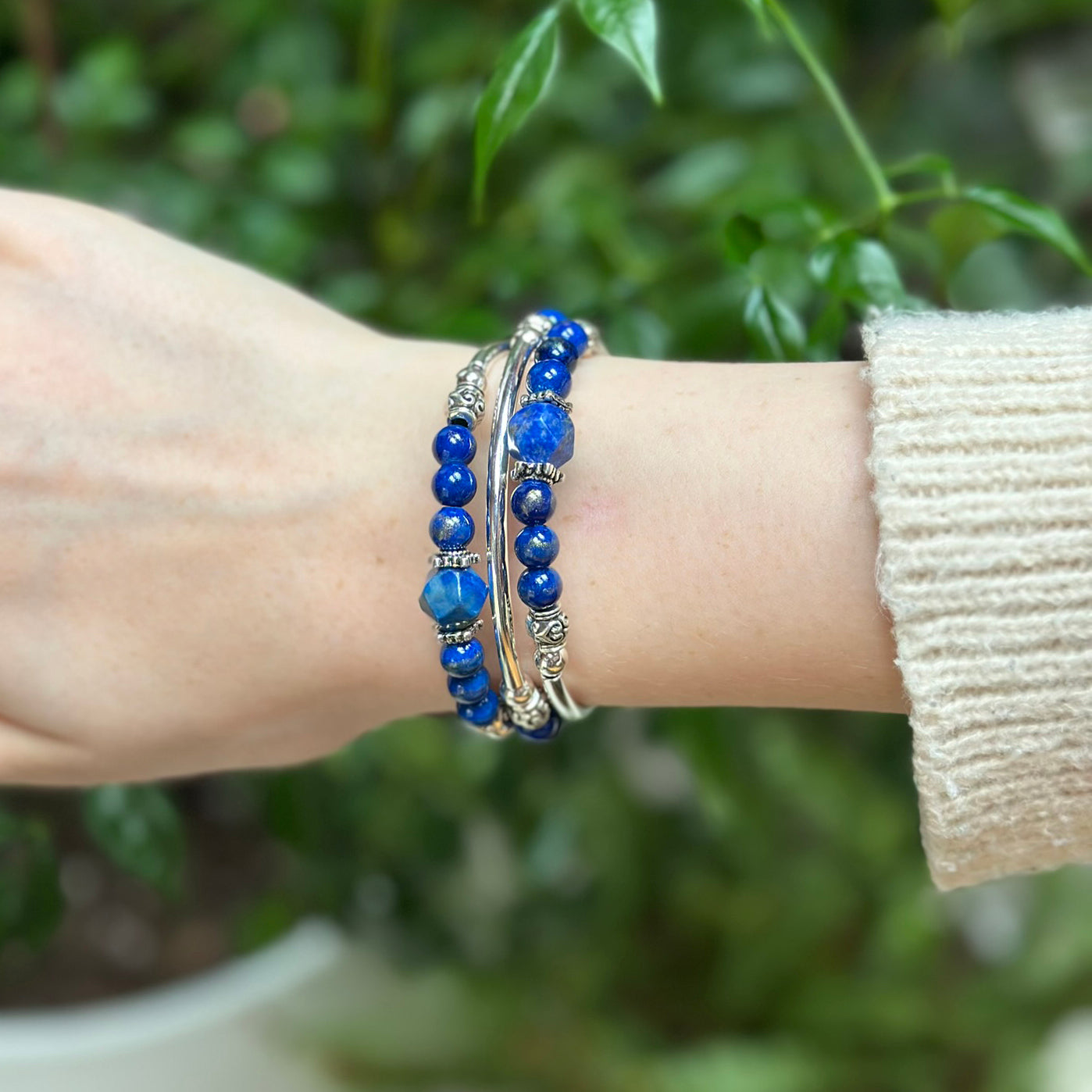 Hand wearing  blue beaded bracelets with a blurred green background