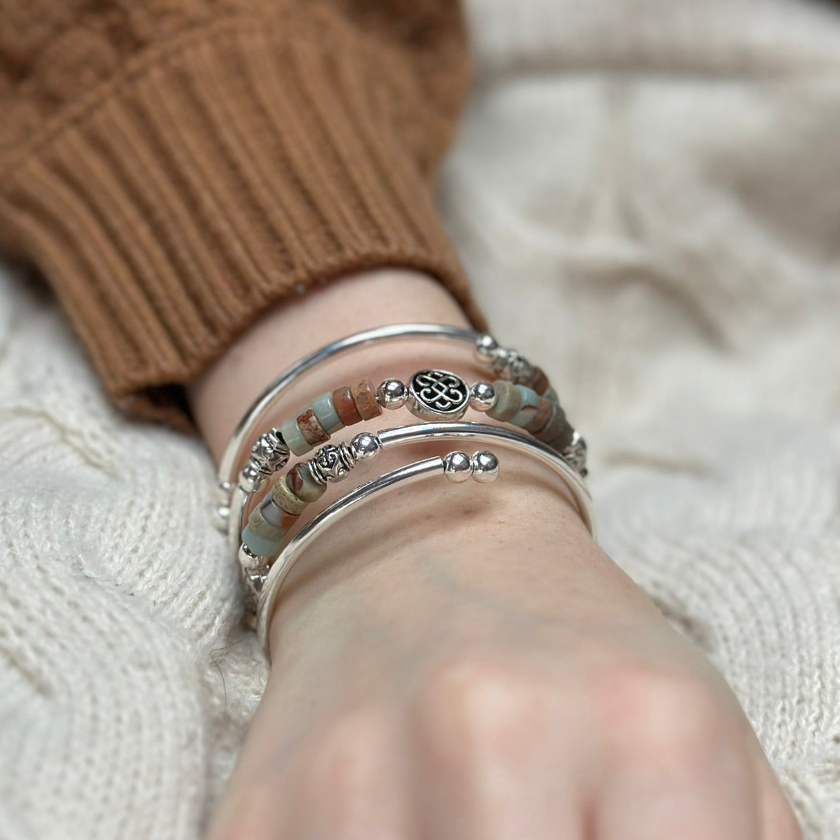 Close-up of a wrist wearing multiple silver bracelets on a textured surface.