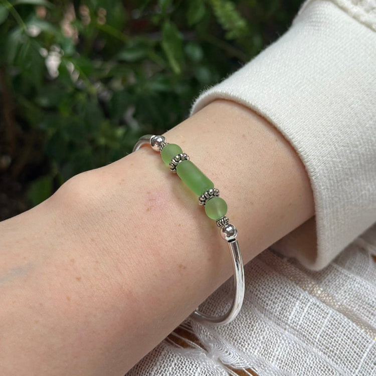 Green beaded bracelet on a wrist with a blurred natural background