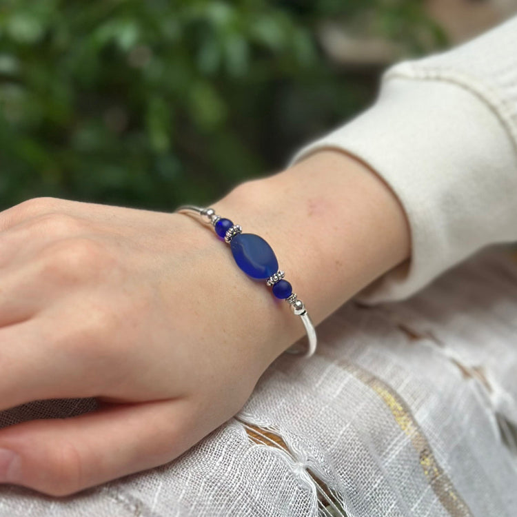 Hand wearing a blue beaded bracelet with a blurred natural background
