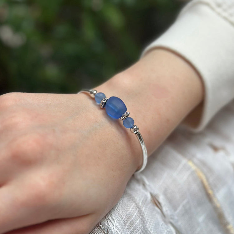 Silver bracelet with blue beads on a wrist against a blurred natural background