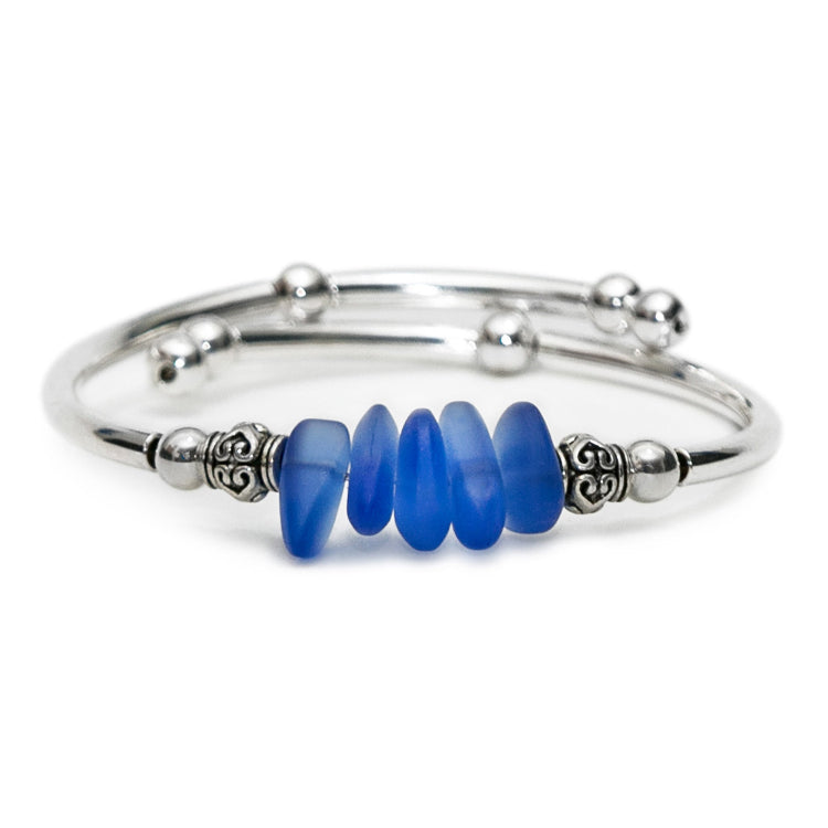 Silver adjustable bangle bracelet featuring stacked sea glass nuggets in blue, accented with decorative silver spacer beads on a clean white background.