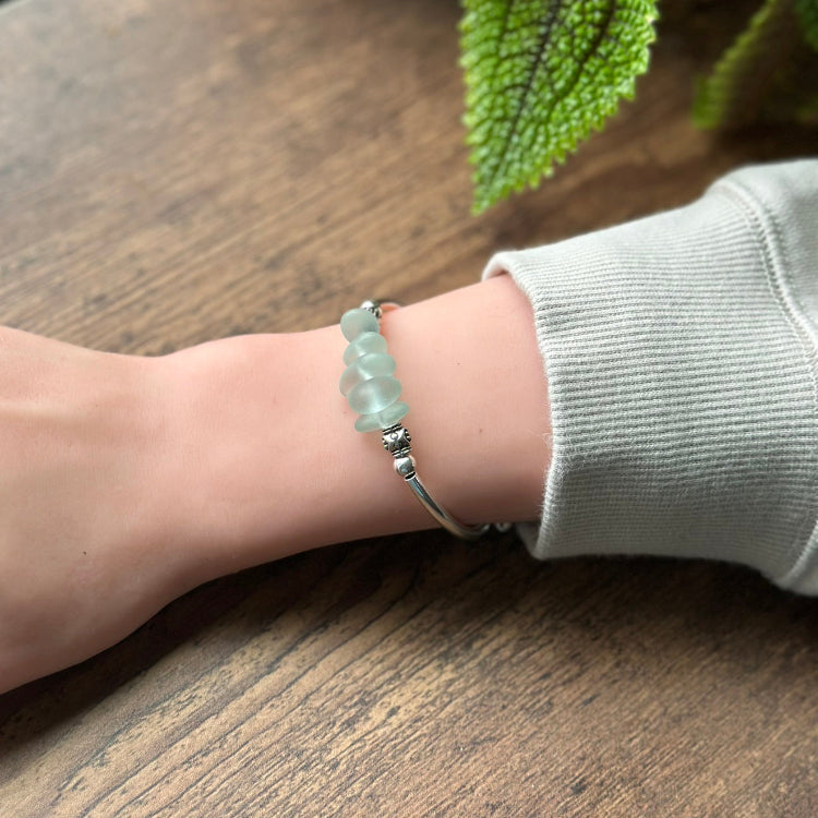 Person wearing a silver bracelet with green beads on a wooden surface