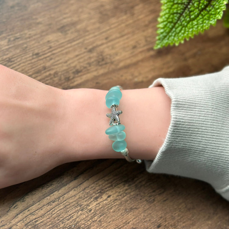 Turquoise beaded bracelet with a starfish charm on a wrist against a wooden background
