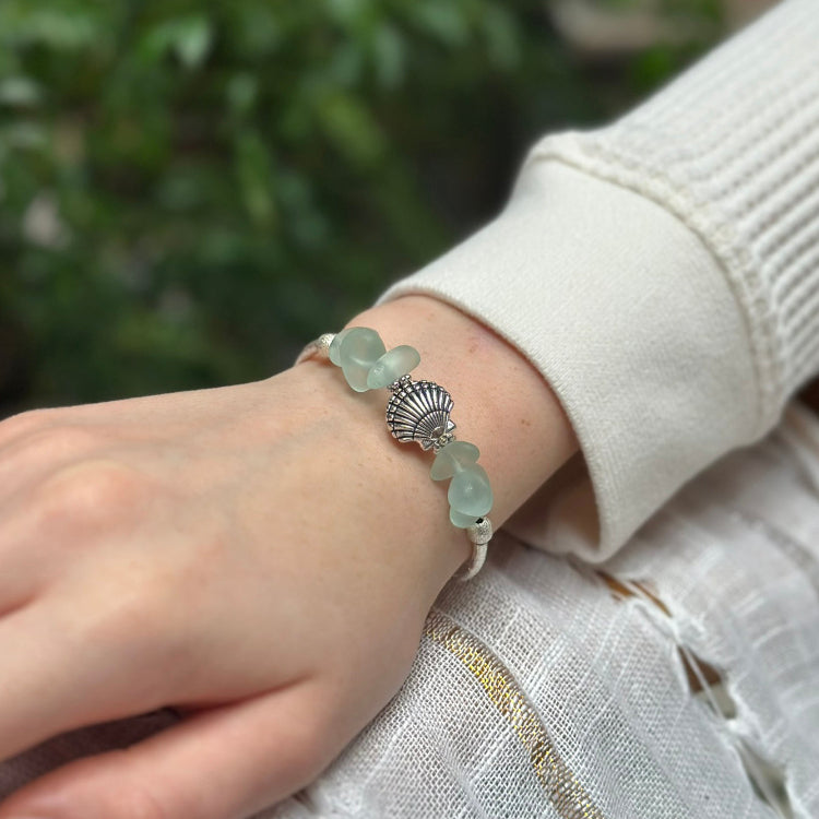 Hand wearing a bracelet with green beads and a silver clasp against a blurred natural background