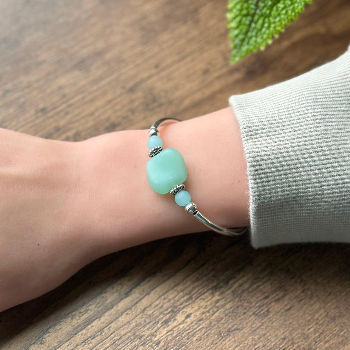 Silver bracelet with frosted seafoam sea glass bead on a wrist with a wood toned background
