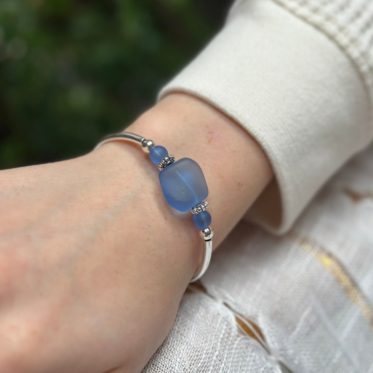 Silver bracelet with frosted sapphire blue sea glass bead on a wrist with a sleeve