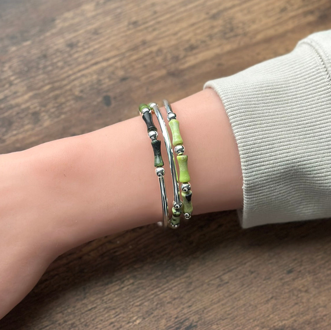 Close-up of a wrist wearing silver and green bracelet on a wooden surface