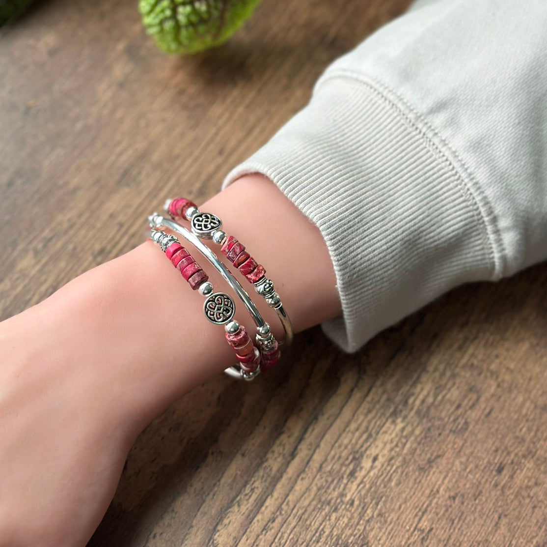 Wrist with pink beaded bracelets on a wooden surface