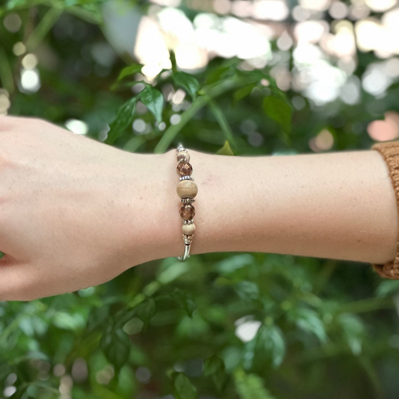 brown and tan bracelet with silver accents on a wrist in front of a greenery background