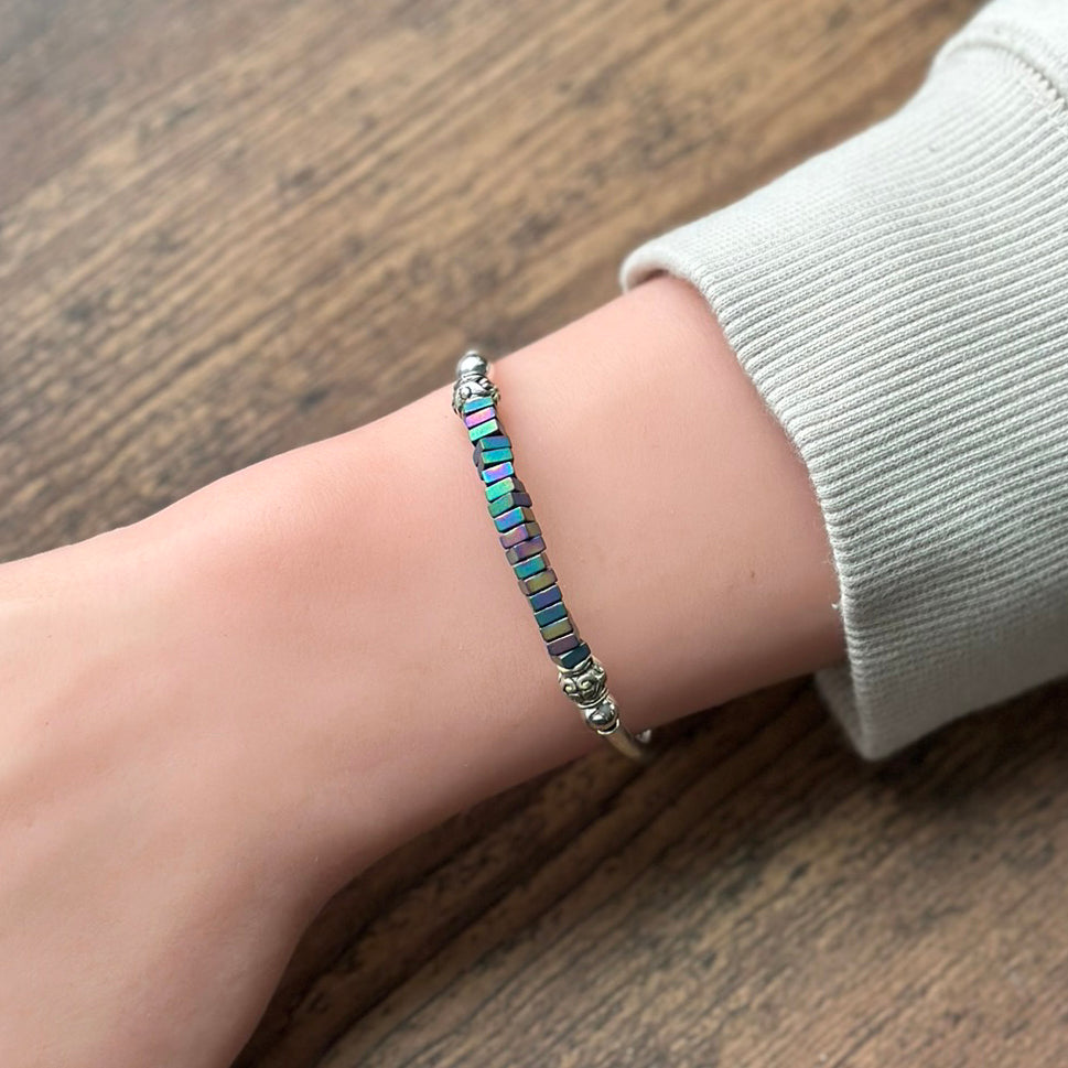 silver bracelet with rainbow square beads on a wrist with a wood background